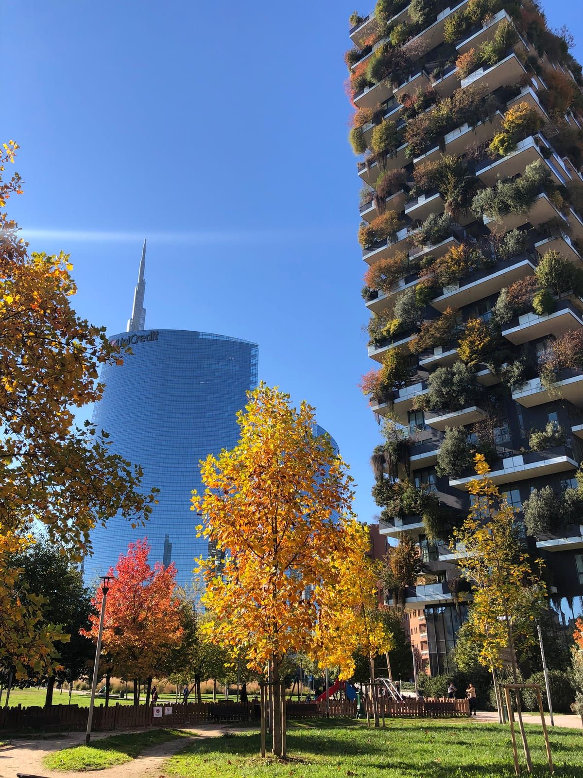 One tower of the Bosco Verticale seen from the park in autumn, with the UniCredit tower behind
