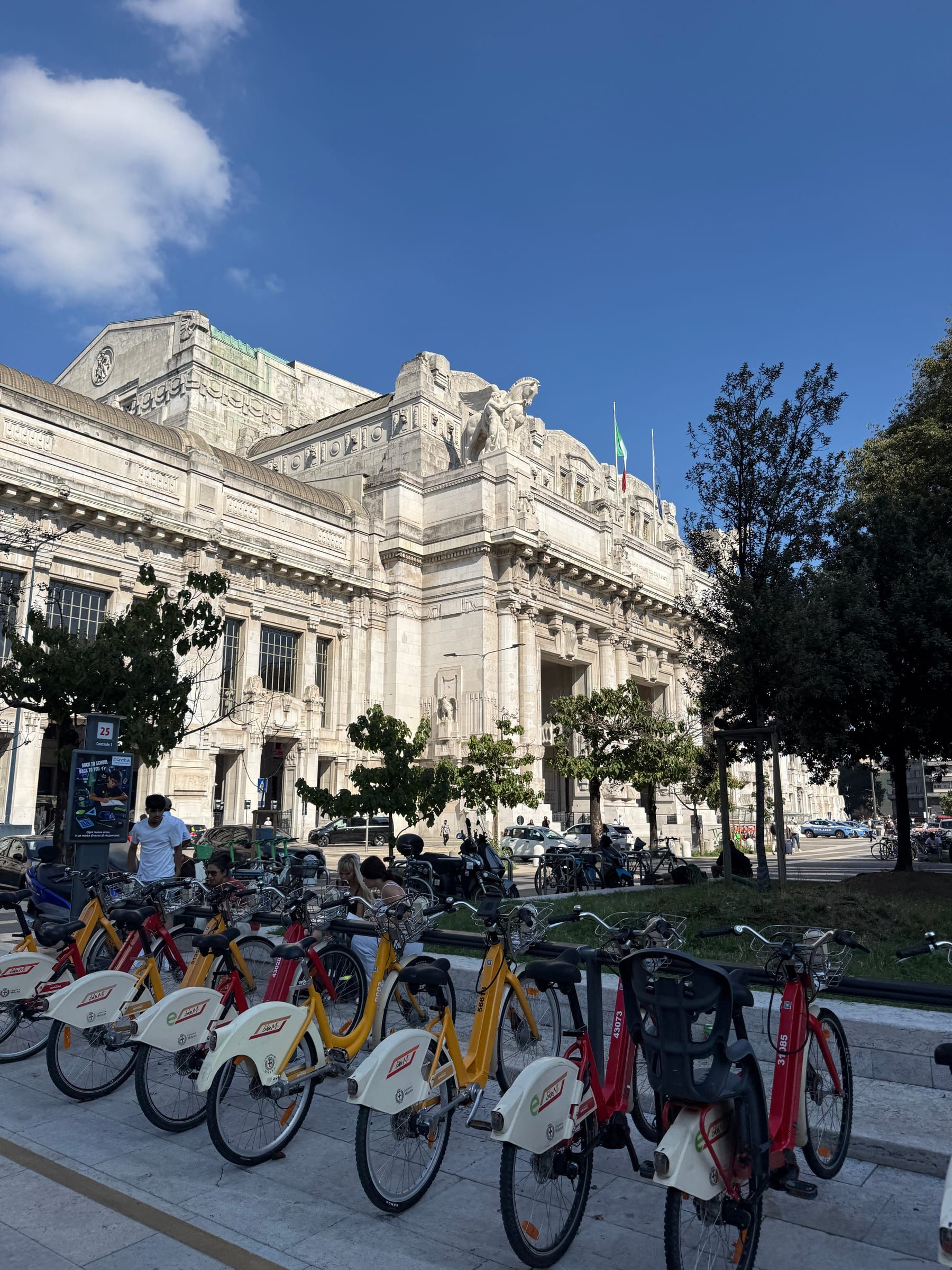 Bike-sharing bicycles lined up in front of the facade of Milano Centrale station