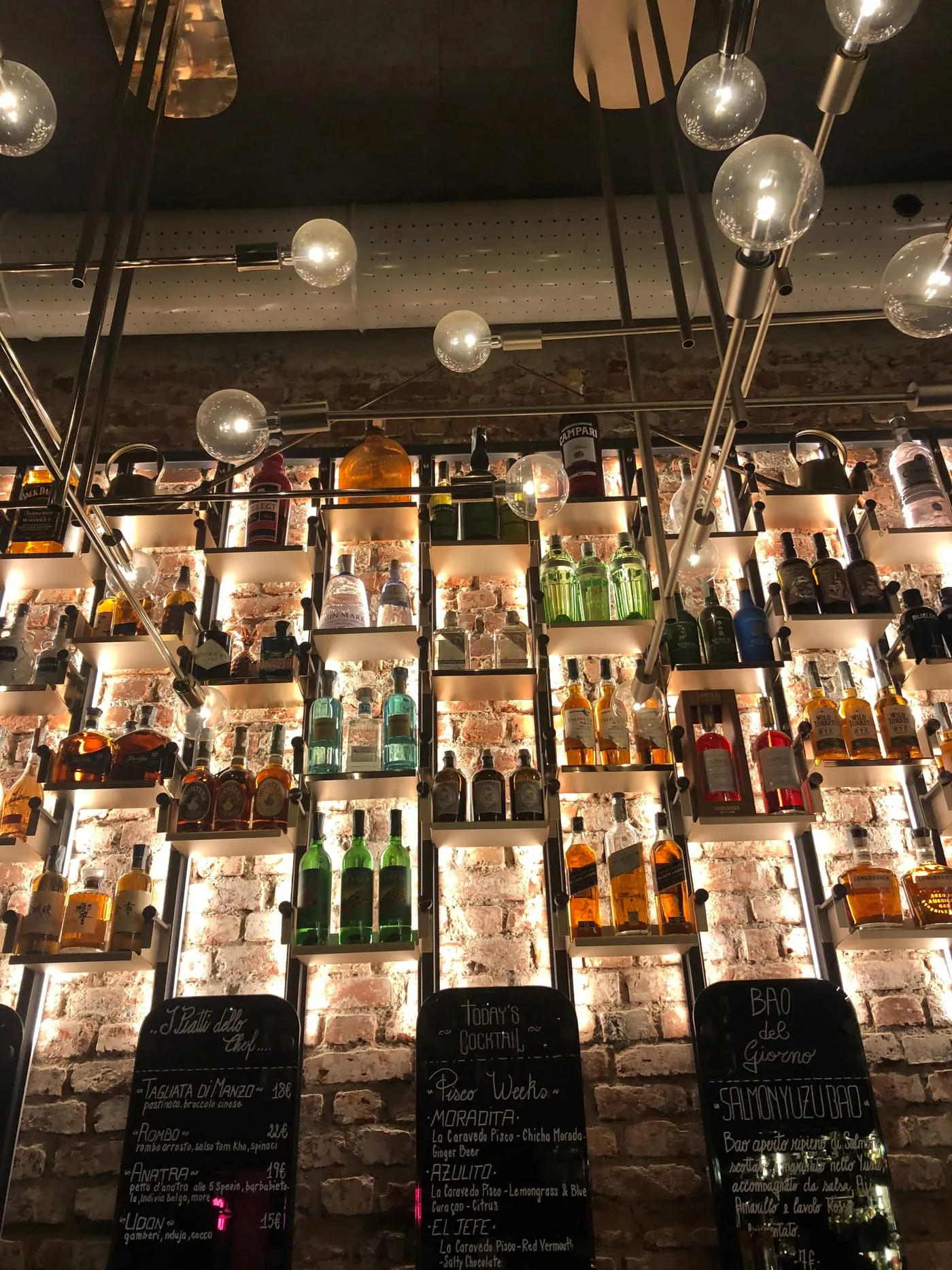 The wall of illuminated bottles behind the bar at BOB, with the cocktail menus written by hand