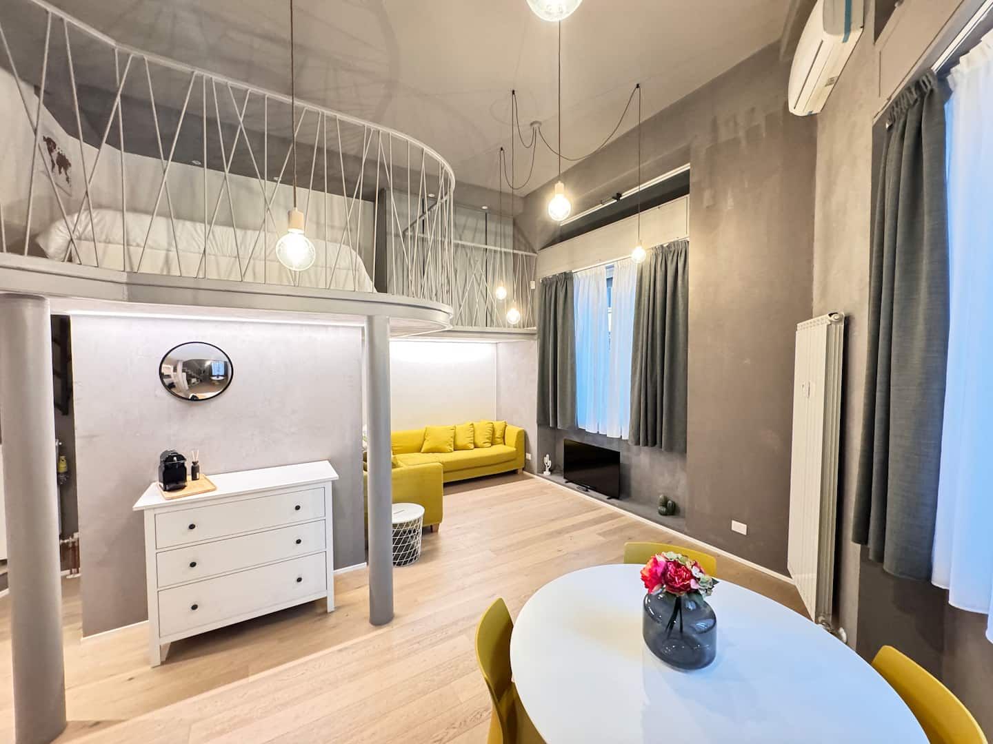 The loft living area, with the round table, the yellow sofa and the mezzanine above