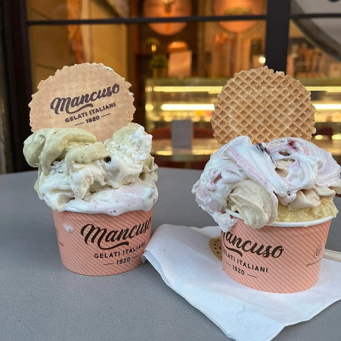 Two cups of Mancuso gelato with a wafer stuck on top, on the little table outside the shop