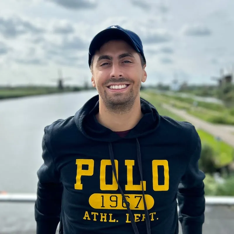 Jacopo Curletto leaning on a railing, wearing a dark hoodie and a cap