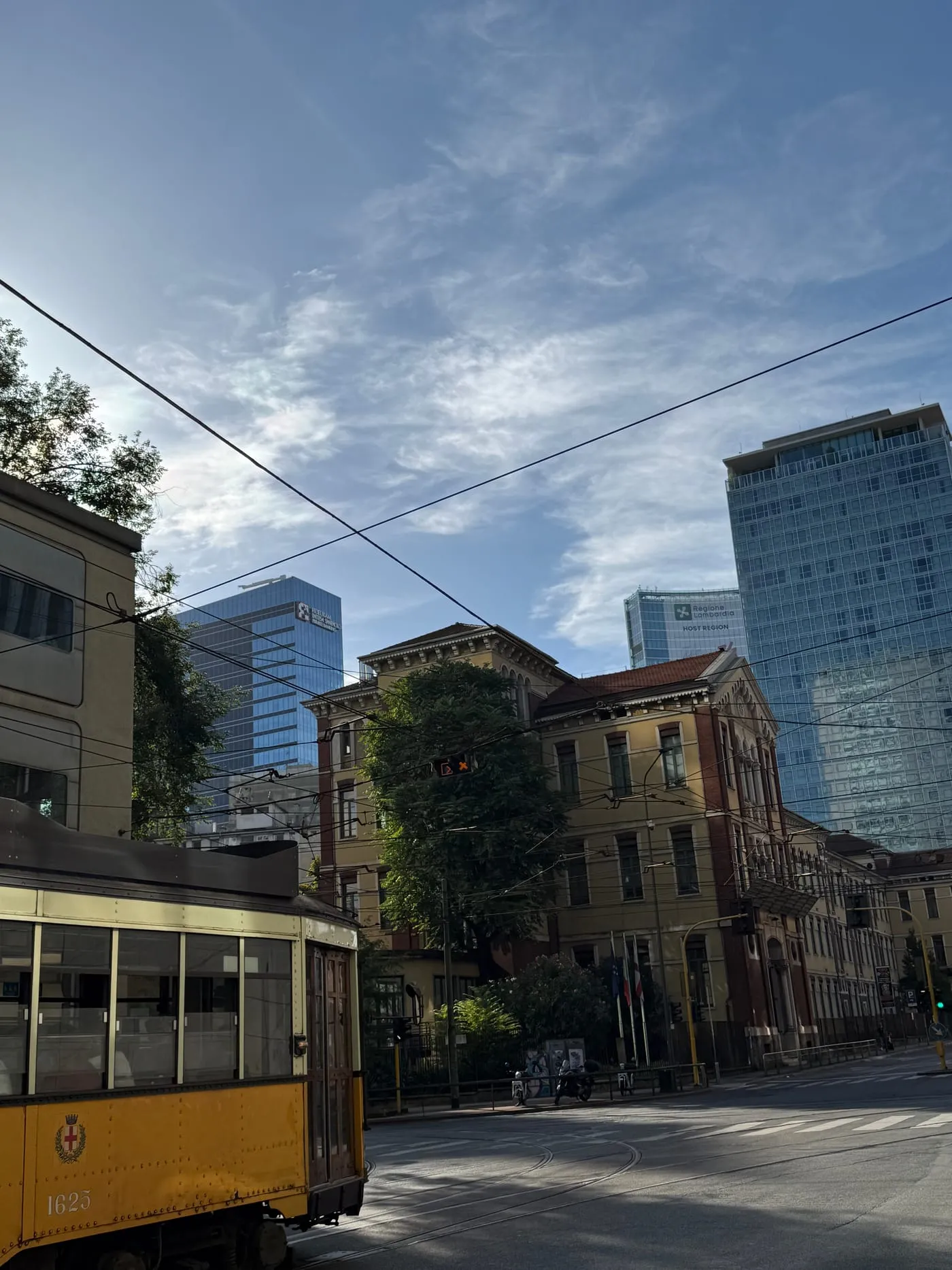 A yellow vintage tram on a street in Isola, with the Porta Nuova skyscrapers in the background